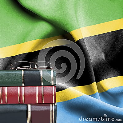 Education concept - Stack of books and reading glasses against National flag of Tanzania Stock Photo