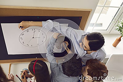 Female teacher explaing clock time to elementary student children in class Stock Photo