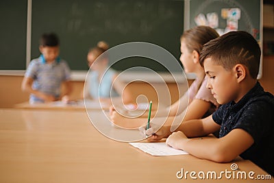 Education, elementary school. Learning and people concept - group of school kids with pens and notebooks writing test in Stock Photo