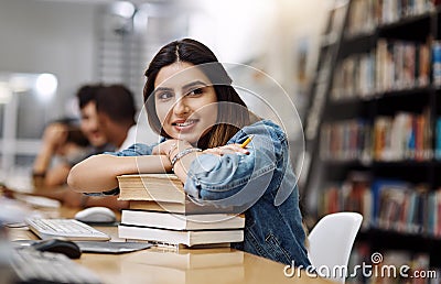 Education gives you endless possibilities in life. a young woman resting on a pile of books in a college library and Stock Photo