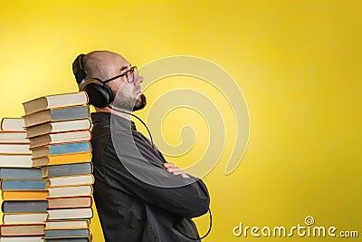 Education and modern technologies. The concept of audio books. A man in glasses, shirt, and earphones leaned against stacks of Stock Photo