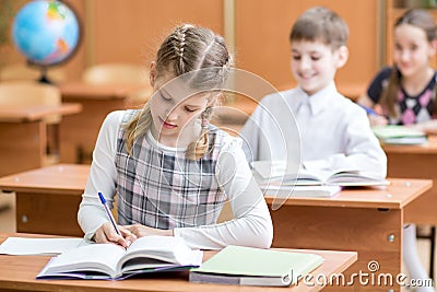 Education, school, learning and children concept - group of school kids with pens and textbooks writing test in classroom Stock Photo