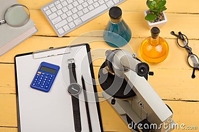 Education and science concept - microscope, book, magnifying glass, calculator, watch, blank clipboard, computer keyboard, eyeglas Stock Photo