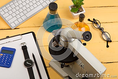 Education and science concept - microscope, book, magnifying glass, calculator, watch, blank clipboard, computer keyboard, eyeglas Stock Photo