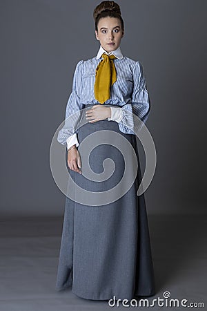 An Edwardian working class woman wearing a striped cotton blouse, mustard yellow cravat, and a grey walking skirt Stock Photo