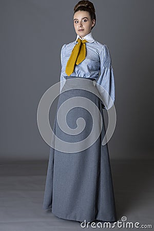 An Edwardian working class woman wearing a striped cotton blouse, mustard yellow cravat, and a grey walking skirt Stock Photo