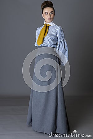 An Edwardian working class woman wearing a striped cotton blouse, mustard yellow cravat, and a grey walking skirt Stock Photo