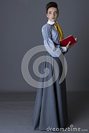 An Edwardian working class woman wearing a striped cotton blouse, mustard yellow cravat, and a grey walking skirt Stock Photo