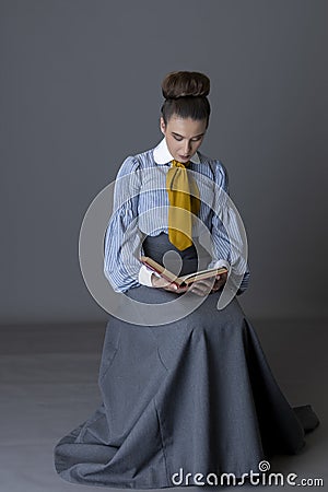 An Edwardian working class woman wearing a striped cotton blouse, mustard yellow cravat, and a grey walking skirt Stock Photo