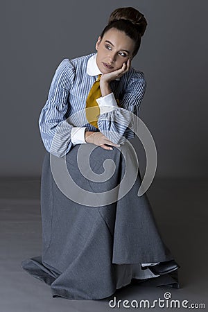 An Edwardian working class woman wearing a striped cotton blouse, mustard yellow cravat, and a grey walking skirt Stock Photo