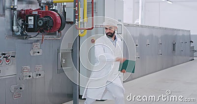Een grappige ingenieur in een grote productiesector die muziek van een draadloze hoofdtelefoon aanbiedt en een kaart vasthoudt stock videobeelden Een grappige ingenieur in een grote productiesector die muziek van een draadloze hoofdtelefoon aanbiedt en een kaart vasthoudt stock videobeelden