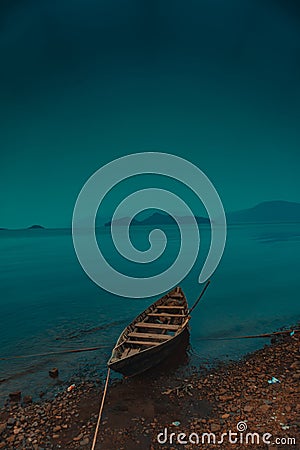 Eerie scenery of an old wooden shallop on the shore of a lake secured with a rope Stock Photo