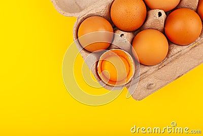 Egg Chicken eggs. Top view of an open gray box with brown eggs on a yellow background. One egg is half broken Stock Photo