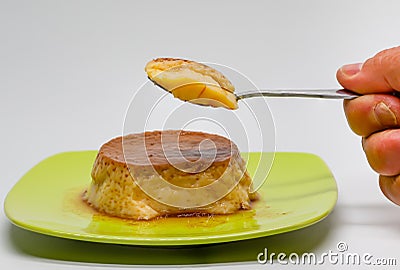 Egg custard on a green plate and a spoon with a piece of custard held in one hand. Sugar desserts. Sugary foods. Stock Photo