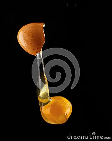 Yolk dropping from cracked raw egg divided Stock Photo