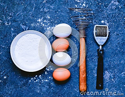 Eggs, flour, kitchen tools on a black concrete table. Ingredient Stock Photo