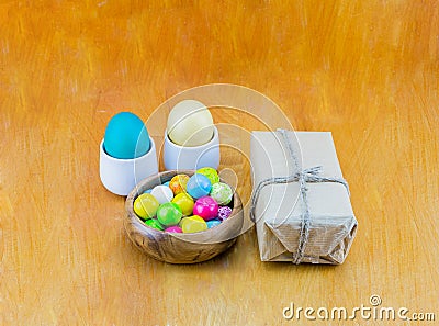 Eggs pastel color sweet chewing gum in a wooden bowl and gift in kraft paper on a wooden table background Stock Photo