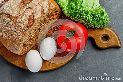 Eggs, tomato, lettuce leaves, bread. Wooden board with Ingredients for cooking. From above Stock Photo
