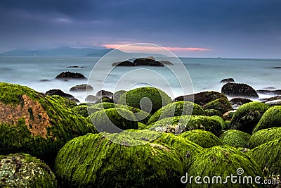 Nature Seascape with Rocks Covered by Green Mosses, Silky Water and Dark Cloudy Sky Stock Photo