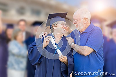 Elated Senior Adult Woman In Cap and Gown Being Congratulated By Husban Stock Photo