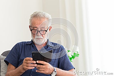 Elder gray beard white hair with glasses looking attention at his smartphone to reading news at home alone Stock Photo