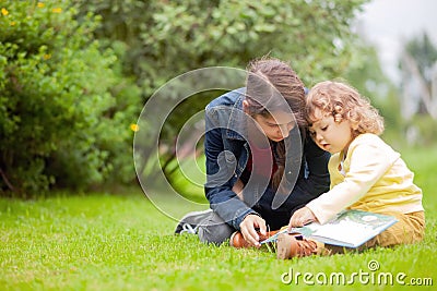 Elder and little sisters reading outdoors in summer day Stock Photo