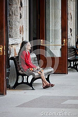 Elder lonely lady at her sixties sits on the bench of a station and waits for someone Editorial Stock Photo