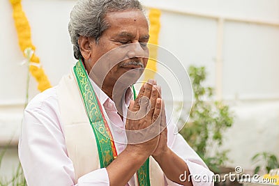 Elder man in closed eyes offering Prayer by namaste gesture praying to god at home in traditional dress during rituals. Stock Photo