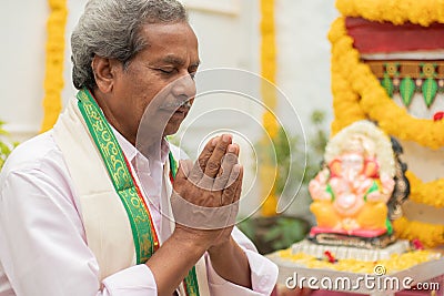 Elder man offering Prayer by namaste gesture in front of Lord Ganesha Idol during Ganesha or vinayaka Chaturthi festival Stock Photo