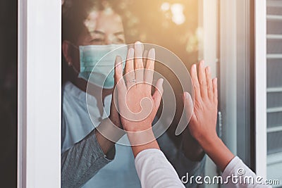 Elderly asian women wearing face mask with hands touching on window to people,Stay at home during coronavirus and covid-19 epidemi Stock Photo