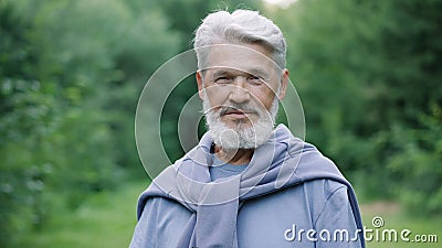 Elderly beard old man portrait in forest nature park. Grandpa face look camera. Stock Photo
