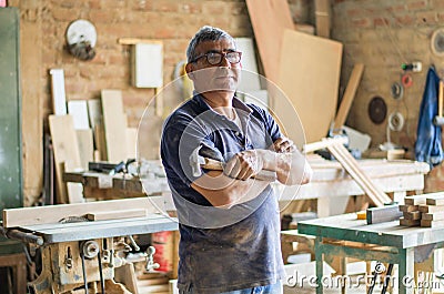 Elderly carpenter posing with crossed arms in his workshop. Stock Photo