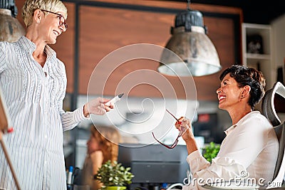 An elderly cheerful business woman talking about a presentation with her female colleague at workplace. Business, office, job Stock Photo