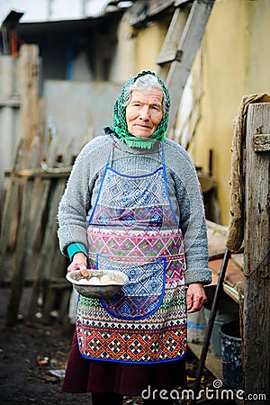 The elderly countrywoman gathers eggs in a hen house. Stock Photo