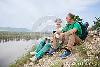 Elderly couple with backpacks travels around mountains. Stock Photo