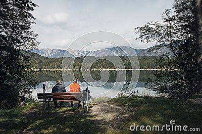 An elderly couple sit on a bench after walking round the lake. Eibsee, Garmisch-Partenkirchen, Bayern, Germany Editorial Stock Photo