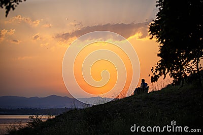 An elderly couple sits on chairs by the lake and looks at the orange sunset. Stock Photo