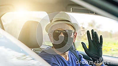 Elderly driver in mask waves left hand in black glove close Stock Photo