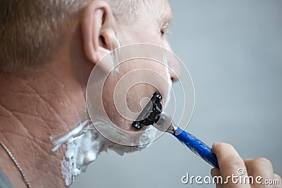 An elderly European man with foam on his face is shaving with a machine. Life of real people Stock Photo