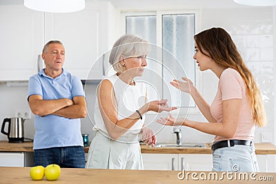 Elderly father tries to calm quarreled wife and daughter in home kitchen Stock Photo