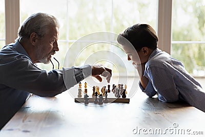 Elderly granddad teaching little boy grandkid to play chess game Stock Photo