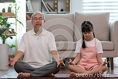 Elderly grandfather and children doing yoga for meditation together in living room at home so happy and comfortable Stock Photo