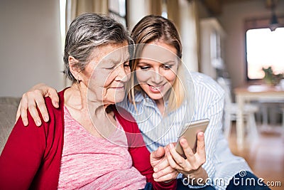Elderly grandmother and adult granddaughter with smartphone at home. Stock Photo