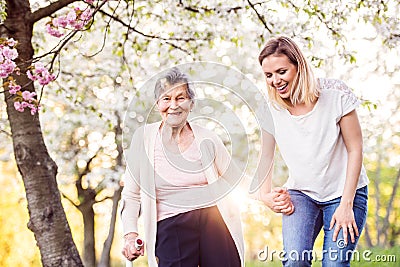 Elderly grandmother with crutch and granddaughter in spring nature. Stock Photo