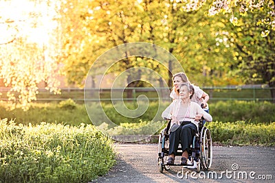 Elderly grandmother in wheelchair with granddaughter in spring nature. Stock Photo