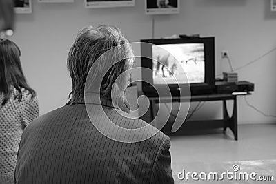 Elderly gray-haired man in jacket watching TV in hall of provincial museum. View from the back Editorial Stock Photo