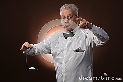 Elderly gray-haired man 50s, in white shirt, glasses and bow tie weighing something on scales with kettlebells Stock Photo
