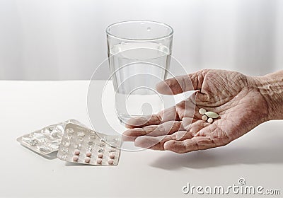 elderly hand of a senior is holding pills, water glass and blister pack on the white table, light background with copy space Stock Photo