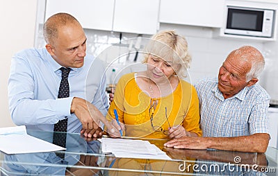 Elderly husband and wife signing agreement papers with bank worker Stock Photo