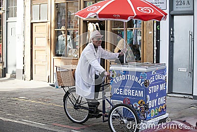 An elderly ice cream seller in a white robe rides a bicycle with his ice cream cart Editorial Stock Photo